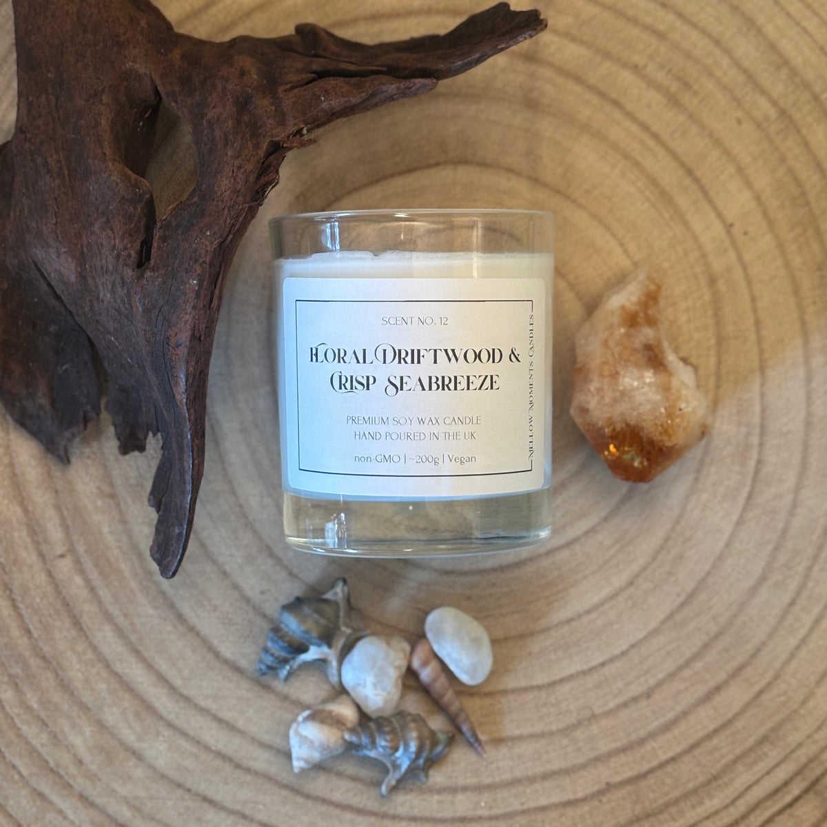 Candle labelled 'Floral Driftwood & Crisp Seabreeze' on a wooden surface with Amber crystal, driftwood, and shells.