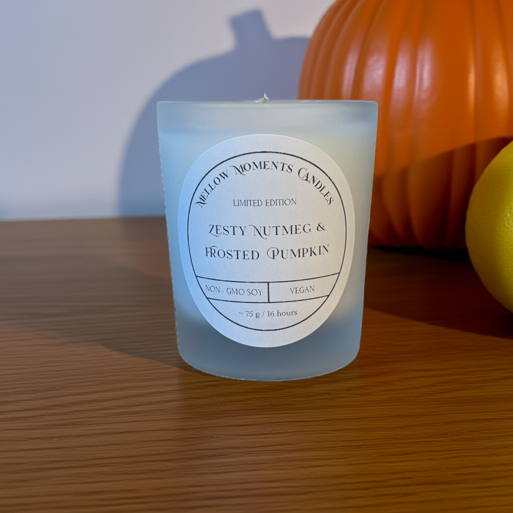 Frosted pumpkin and nutmeg labelled candle with a pumpkin and lemon in the background on a wooden surface