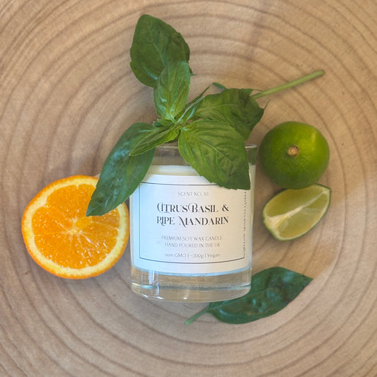 Candle labeled 'Citrus Basil & Ripe Mandarin' with an orange, lime, and basil leaves on a wooden surface.