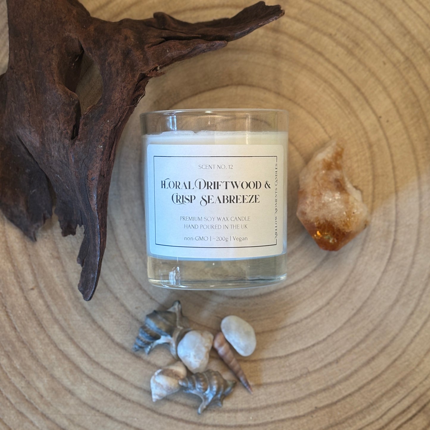 Candle labelled 'Floral Driftwood & Crisp Seabreeze' on a wooden surface with Amber crystal, driftwood, and shells.