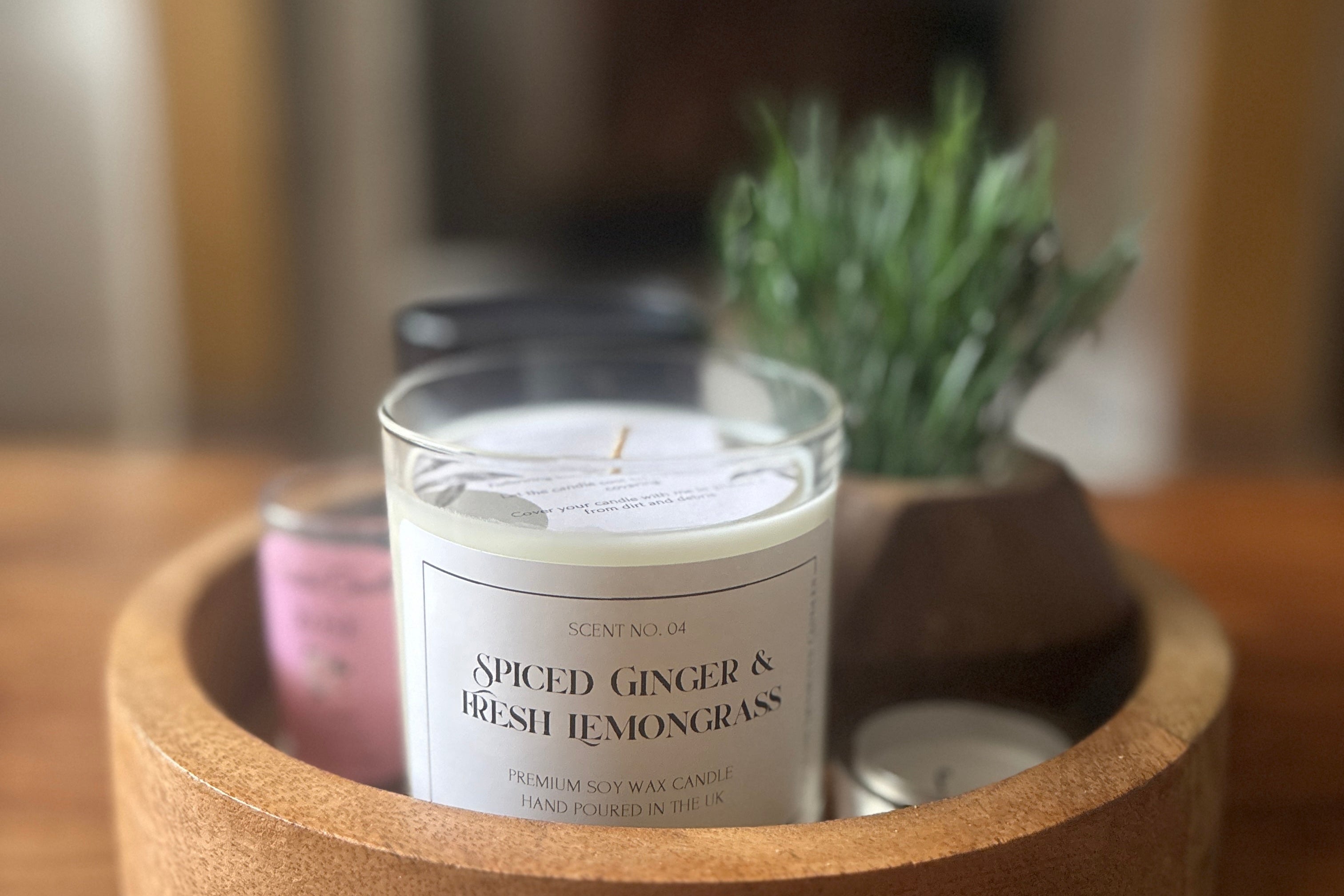 Candle scented with 'Spiced Ginger & Fresh Lemongrass' on a wooden tray with a blurred background of a homely environment