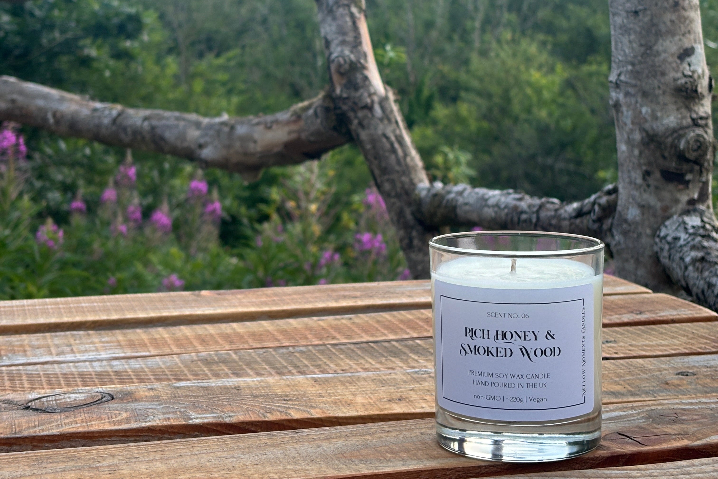 A soy wax candle scented honey and wood on a wooden surface with a natural plant background