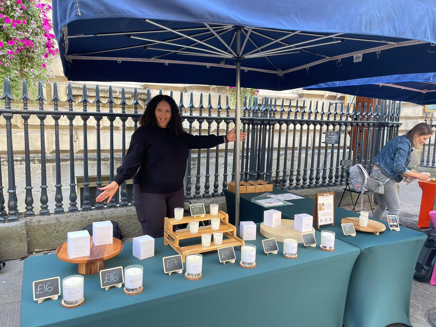 Mellow moments candles founder standing behind a market table with soy candles and small signs under a blue canopy at St NIcks Market