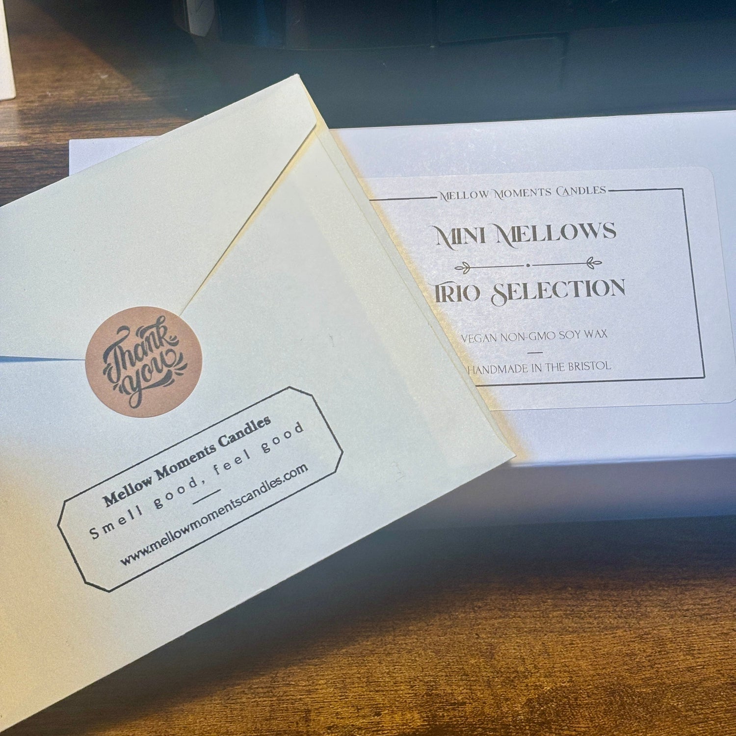 Envelope with Mellow Moments Candles branding on a thankyou gift note; in front of three mini candles gift box