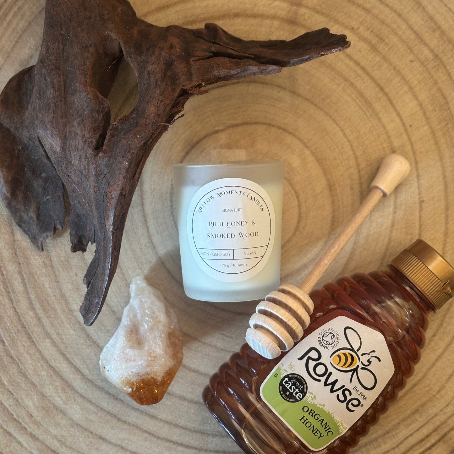 Frosted candle labelled "Rich honey & smoked wood" with cedarwood, amber crystal, honey, and a honey dipper on a wooden surface