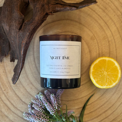 Candle labeled 'Night Time' on a wooden surface with a lemon, wood, and lavender.