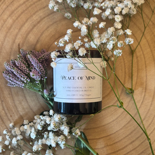 Candle labeled 'Peace of Mind' surrounded by white flowers and lavender on a wooden surface