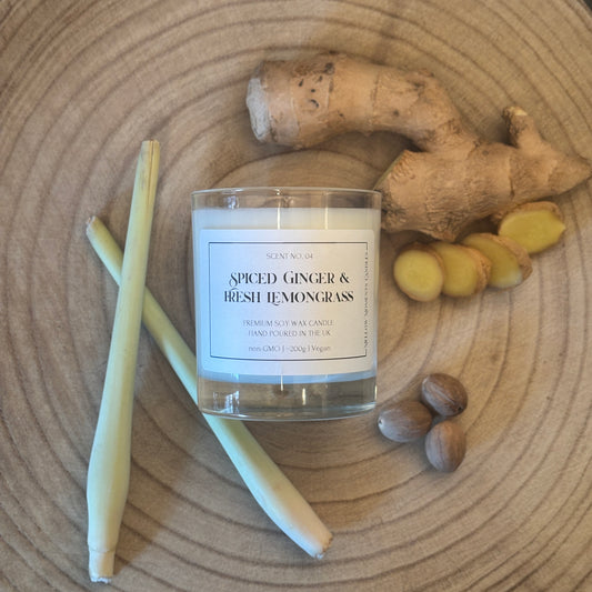 Candle labelled 'Spiced Ginger & Fresh Lemongrass' with ginger root, nutmeg, and lemongrass stalks on a wooden surface