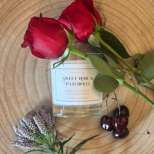 Candle labeled 'Sweet Rose & Patchouli' with red roses, cherries, and lavender on a wooden surface